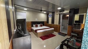 Quarto de hotel com cama, televisão, escrivaninha, chuveiro e banheiro.
