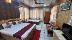 A hotel room with a bed, a sofa, a TV, a ceiling fan, and curtains. - Hotel Ekant Lodge (Dharamshala)