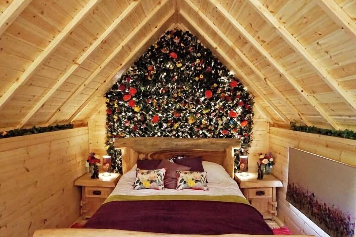 Un dormitorio acogedor en el ático, con techo de listones de madera, una cama con almohadas estampadas y un banco rústico.