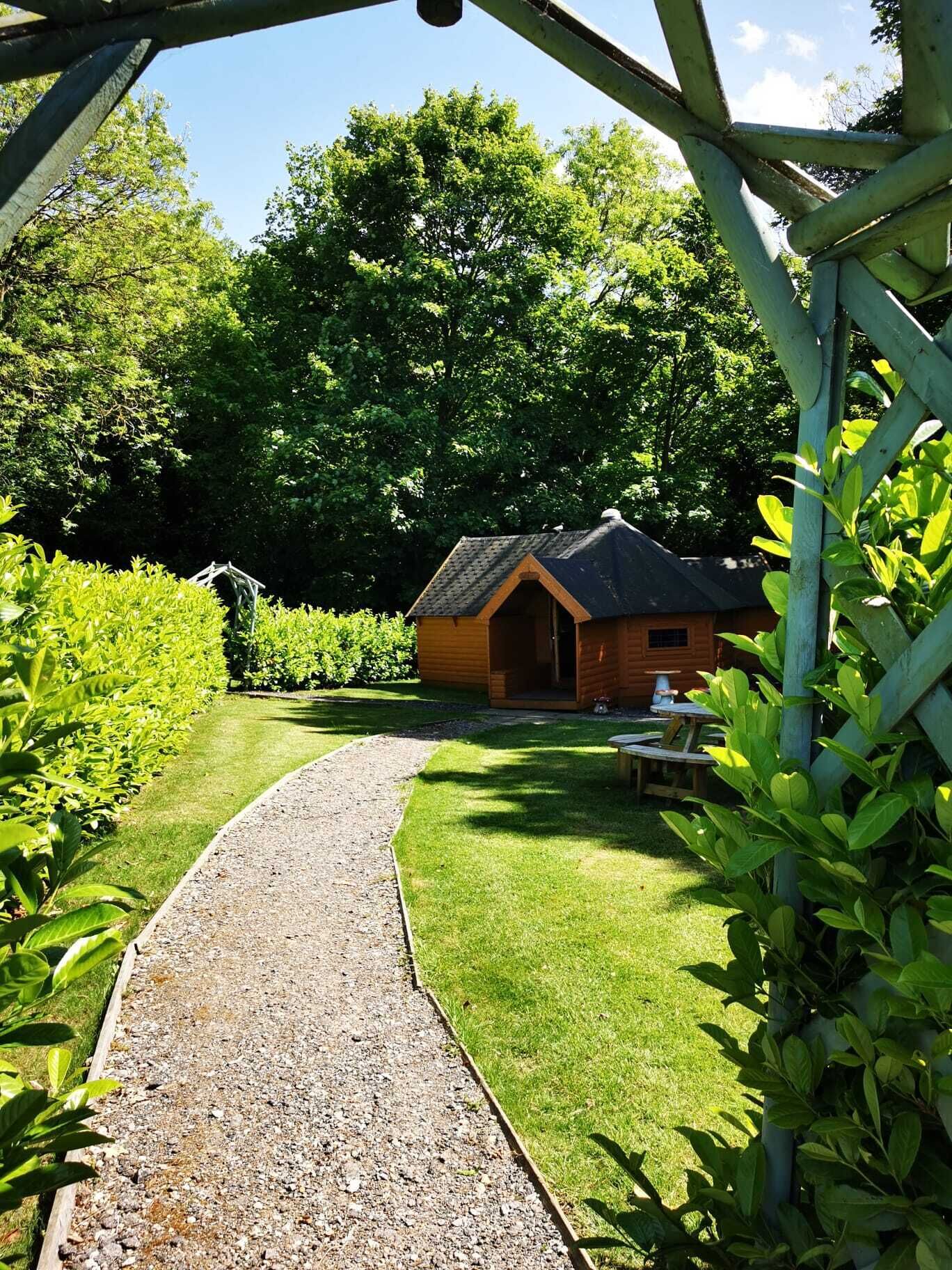A wooden cabin with a gravel path leading to it, surrounded by lush greenery and trees.