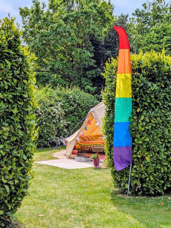 Une tente ornée d’un drapeau aux couleurs de l’arc-en-ciel, dans un jardin.