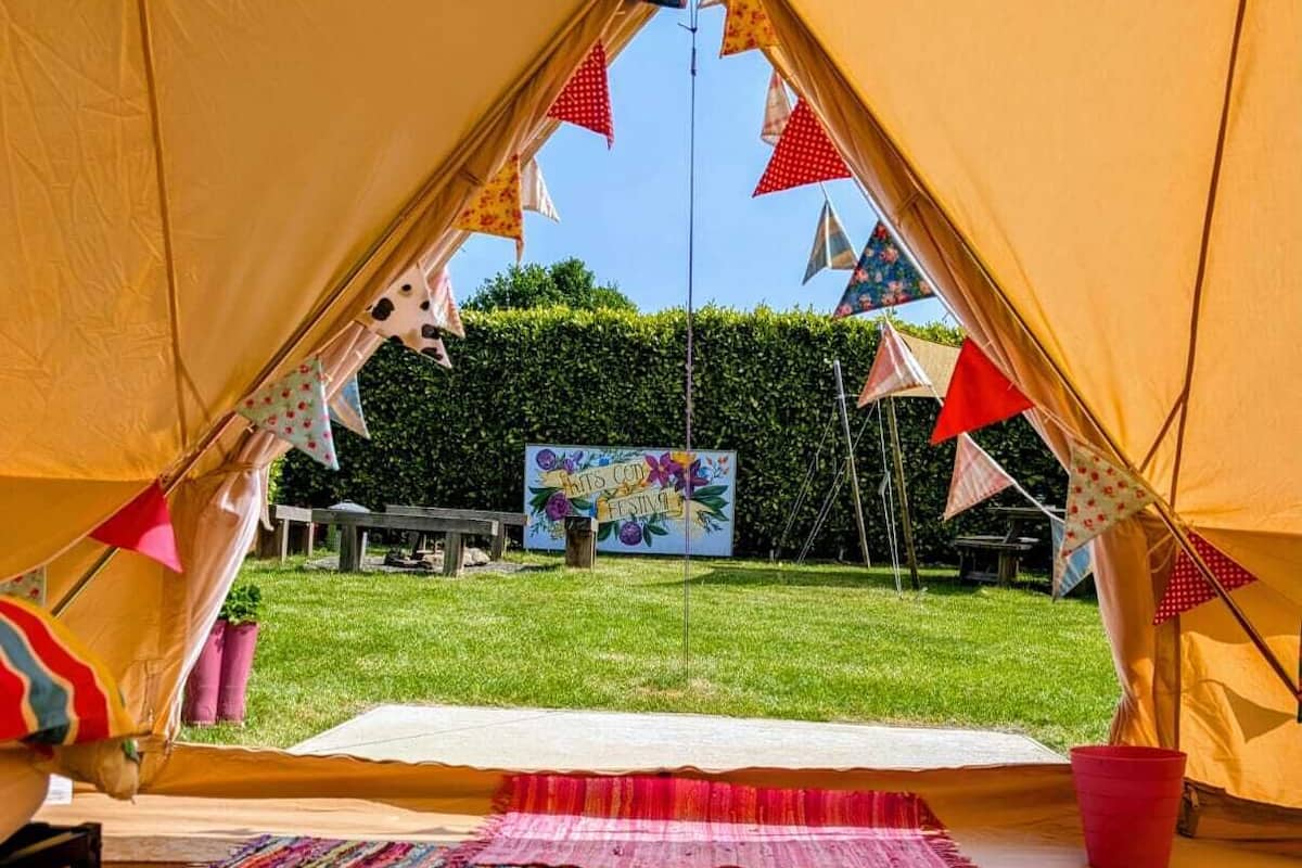 Una carpa con una alfombra interior de rayas coloridas, un letrero al fondo y un área verde afuera.