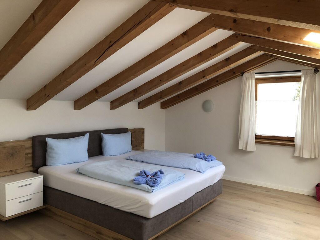 Ein Schlafzimmer mit Holzboden, einem großen Bett mit blauer Bettwäsche, einem Nachttisch und einem Fenster mit Vorhängen.