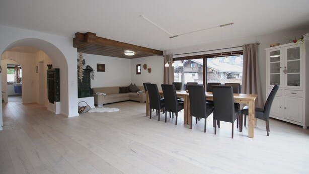 Uma sala de estar ampla com uma mesa de jantar, cadeiras, um sofá e um armário.