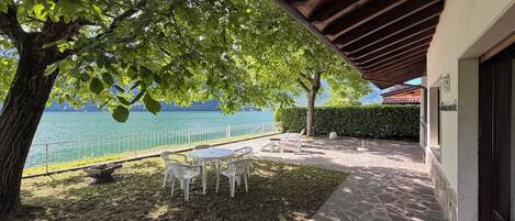 Eine Terrasse mit Tisch und Stühlen, ein Steinweg und Blick aufs Wasser.
