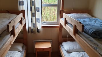 Habitación tipo dormitorio con dos literas, una mesita de madera y una ventana con cortinas.
