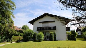 A two-story house with a balcony, surrounded by a well-maintained lawn and trees.