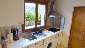 Eine kompakte Küche mit integriertem Waschtrockner, einer Kaffeemaschine und einem Fenster mit Blick auf Grünflächen.