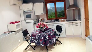 Eine kompakte Küche mit weißen Schränken, einem eingebauten Backofen, einer Mikrowelle und einem Fenster mit Bergblick.