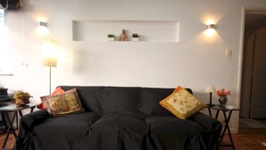 Ein schwarzes Sofa mit bunten Kissen, ein kleines Regal mit Dekoration und zwei Wandlampen.