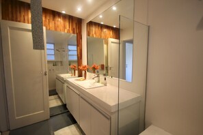 A modern bathroom with a white vanity, two sinks, a large mirror, and wooden paneling on the ceiling. - Gohouse - Prudente 301 A (Rio de Janeiro)