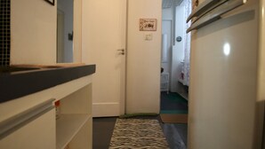 Ein schmales Dielenkorridor mit einem zebraartig gemusterten Teppich, einer weißen Tür und einem Kühlschrank auf der rechten Seite.