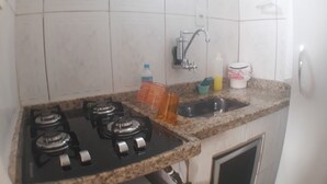 A kitchen with a gas stove, a sink, and a faucet. There are cleaning supplies and a water bottle on the counter. - Gohouse - Laranjeiras 116 (Rio de Janeiro)