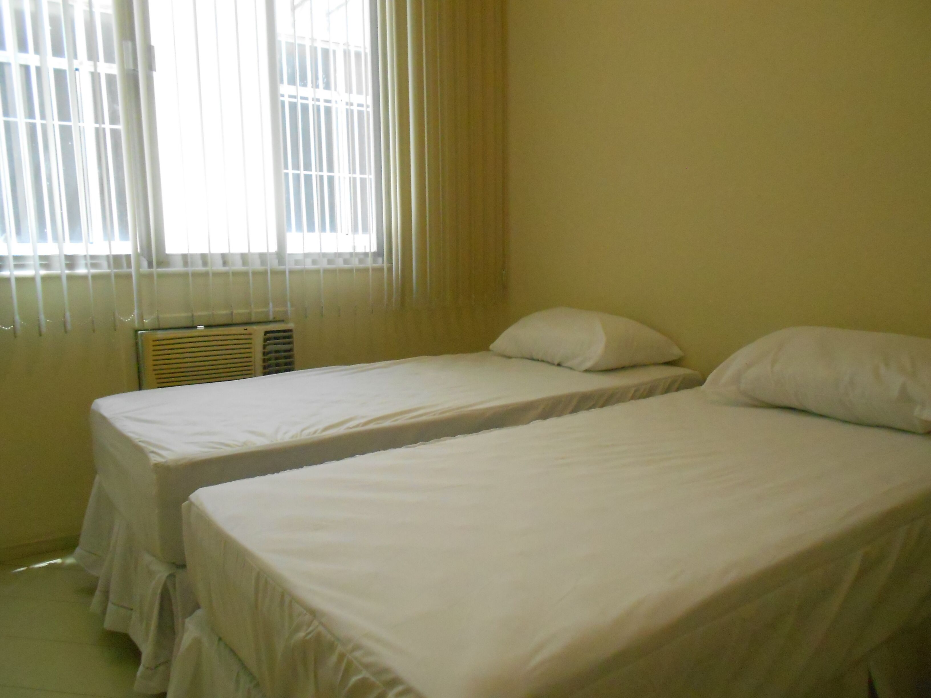 A room with two single beds, a window with blinds, and a radiator.