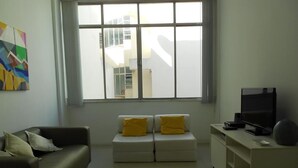 A modern living room with a sofa, ottoman, and TV stand. - Gohouse - Copacabana 1206 (Rio de Janeiro)