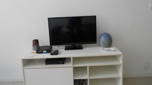 A white entertainment unit with a flat-screen TV, a remote control, and a small decorative item. - Gohouse - Copacabana 1206 (Rio de Janeiro)