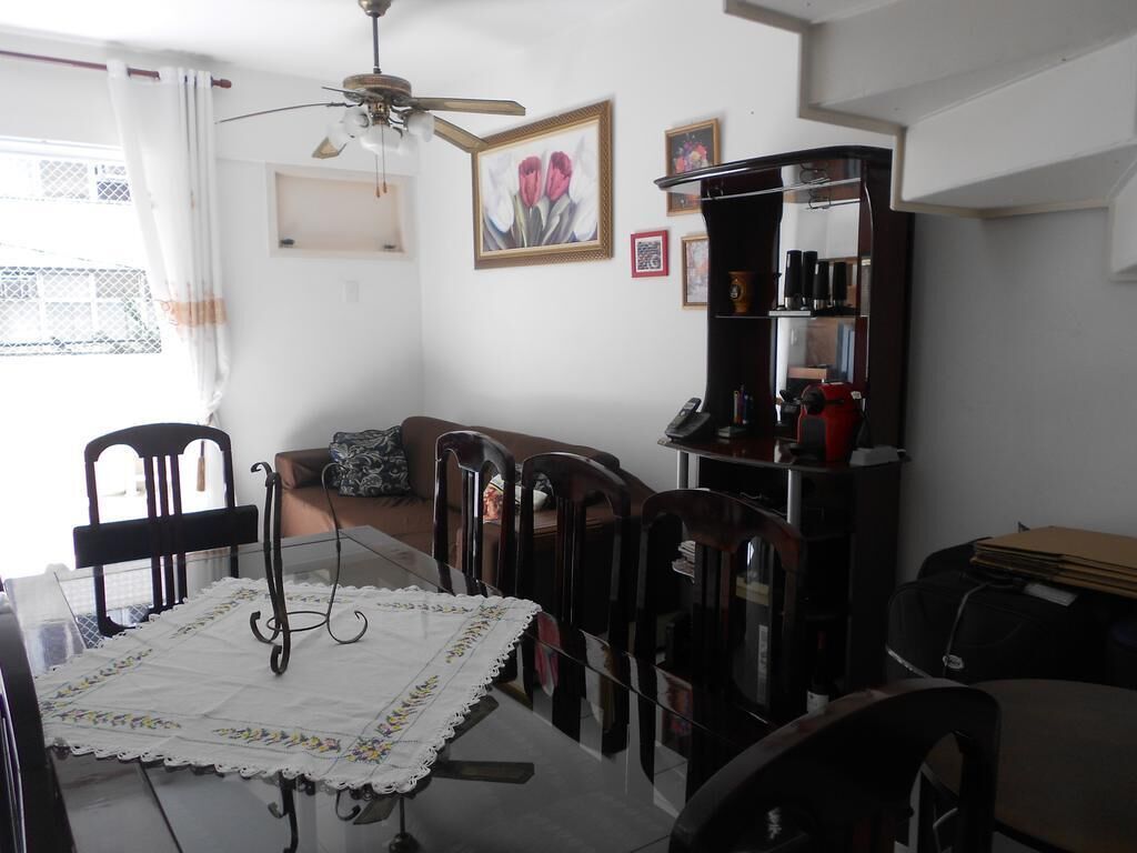 A dining area with a glass table, chairs, a ceiling fan, and a bookshelf with various items.