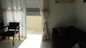 A living room with a sofa, a chair, and a sliding glass door leading to a balcony. - Gohouse - Dutra 102 (Rio de Janeiro)