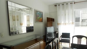 A room with a TV, wooden cabinet, dining table, chairs, and a large mirror. - Gohouse - Dutra 102 (Rio de Janeiro)