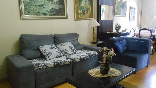 A living room with a grey sofa, a coffee table with a vase, and a painting of a seascape. - Gohouse - Figueiredo 601 (Rio de Janeiro)