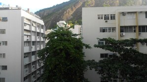 A multi-story building with balconies and air conditioning units, surrounded by trees and a mountain in the background. - Gohouse - Figueiredo 601 (Rio de Janeiro)