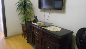 A room with a wooden cabinet, a television mounted on the wall, a potted plant, and a chair. - Gohouse - Figueiredo 601 (Rio de Janeiro)