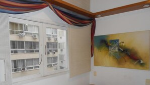 A room with a bed, a window with blinds, an air conditioning unit, and a colorful abstract painting on the wall. - Gohouse - Figueiredo 303 (Rio de Janeiro)