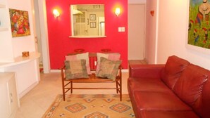 A living room with a red accent wall, a wooden sofa, a patterned rug, and a painting on the wall. - Gohouse - Figueiredo 303 (Rio de Janeiro)