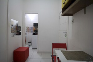 A narrow hallway with a red bench, a table with a woven table runner, and a kitchen area visible through an open door. - Gohouse - Raul 607 (Rio de Janeiro)