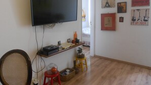 A living room with a flat-screen TV mounted on the wall, a wooden floor, and a small table with various items. - Gohouse - Raul 1003 (Rio de Janeiro)
