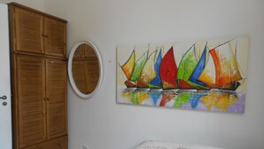 A bedroom with a wooden wardrobe, a round mirror, and a colorful sailboat painting on the wall. - Gohouse - Raul 1003 (Rio de Janeiro)
