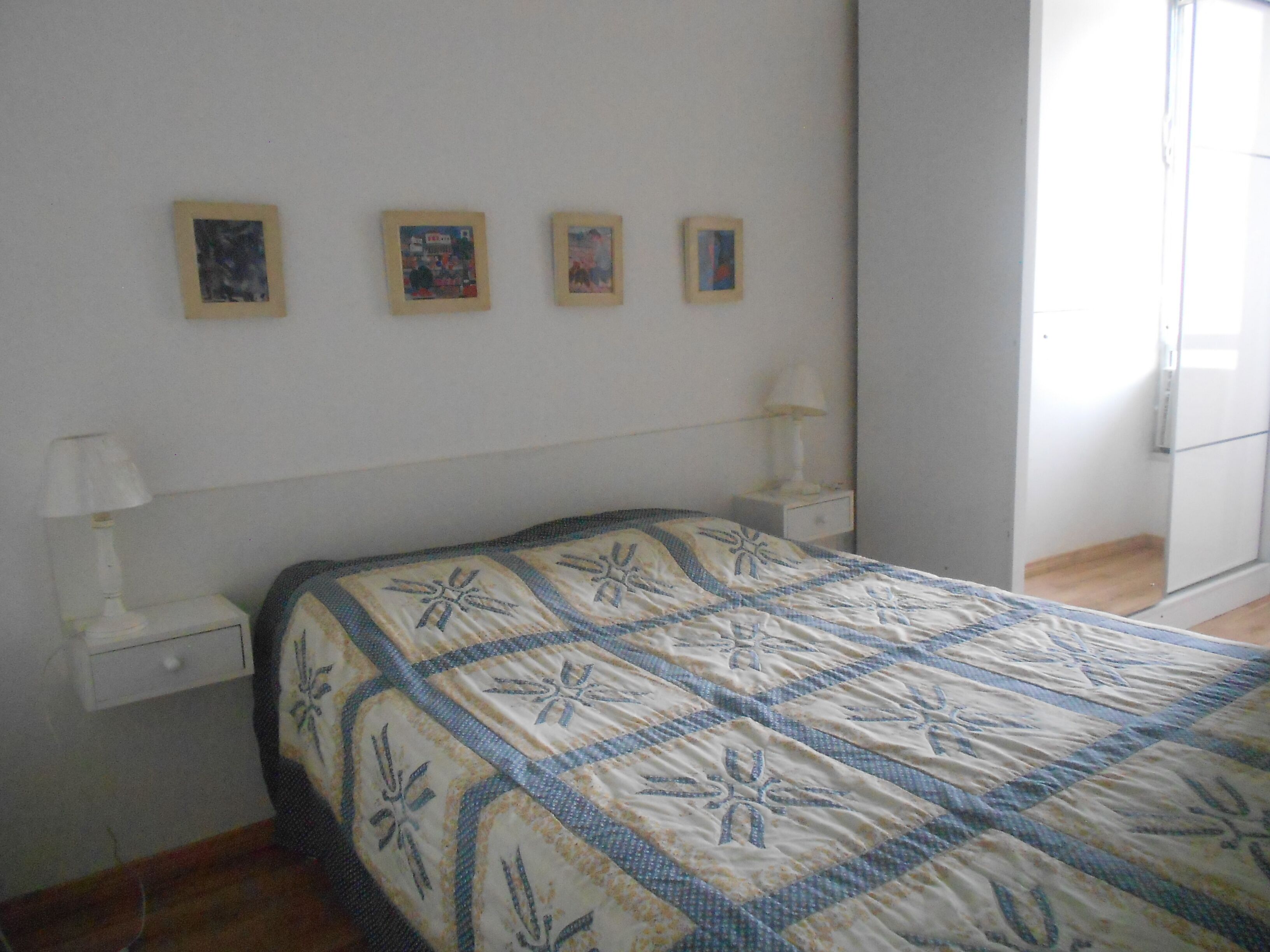 A bedroom with a bed, a nightstand, a lamp, and four framed pictures on the wall.