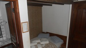 A small, single-bed room with a wooden headboard, a tiled shower area, and a wooden door. - Gohouse - Suite Tonelero 03 (Rio de Janeiro)