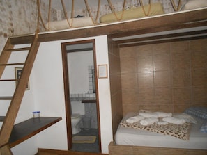 Une chambre avec un lit superposé, une petite échelle en bois, un petit tabouret et un lit simple recouvert d’une couverture à motifs léopard.