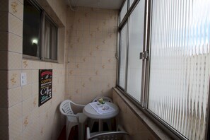 Un petit balcon avec une table et des chaises, une fenêtre avec des stores et une enseigne publicitaire pour le café.