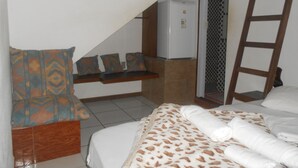 A bedroom with a bed, a bench with pillows, a refrigerator, and a ladder. - Gohouse - Suite Tonelero 02 (Rio de Janeiro)