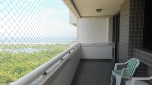 Un balcone con vista su vegetazione e acqua, pareti rivestite di piastrelle bianche e due sedie bianche con strisce rosse.