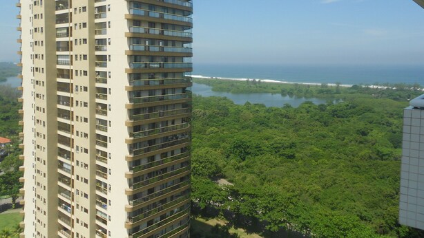 Un edificio alto con numerosi balconi, immerso nel verde e con vista sull'oceano.