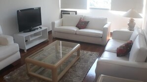 A living room with a flat-screen TV, white sofas, a glass coffee table, and a lamp. - Gohouse - Gomes 202 (Rio de Janeiro)