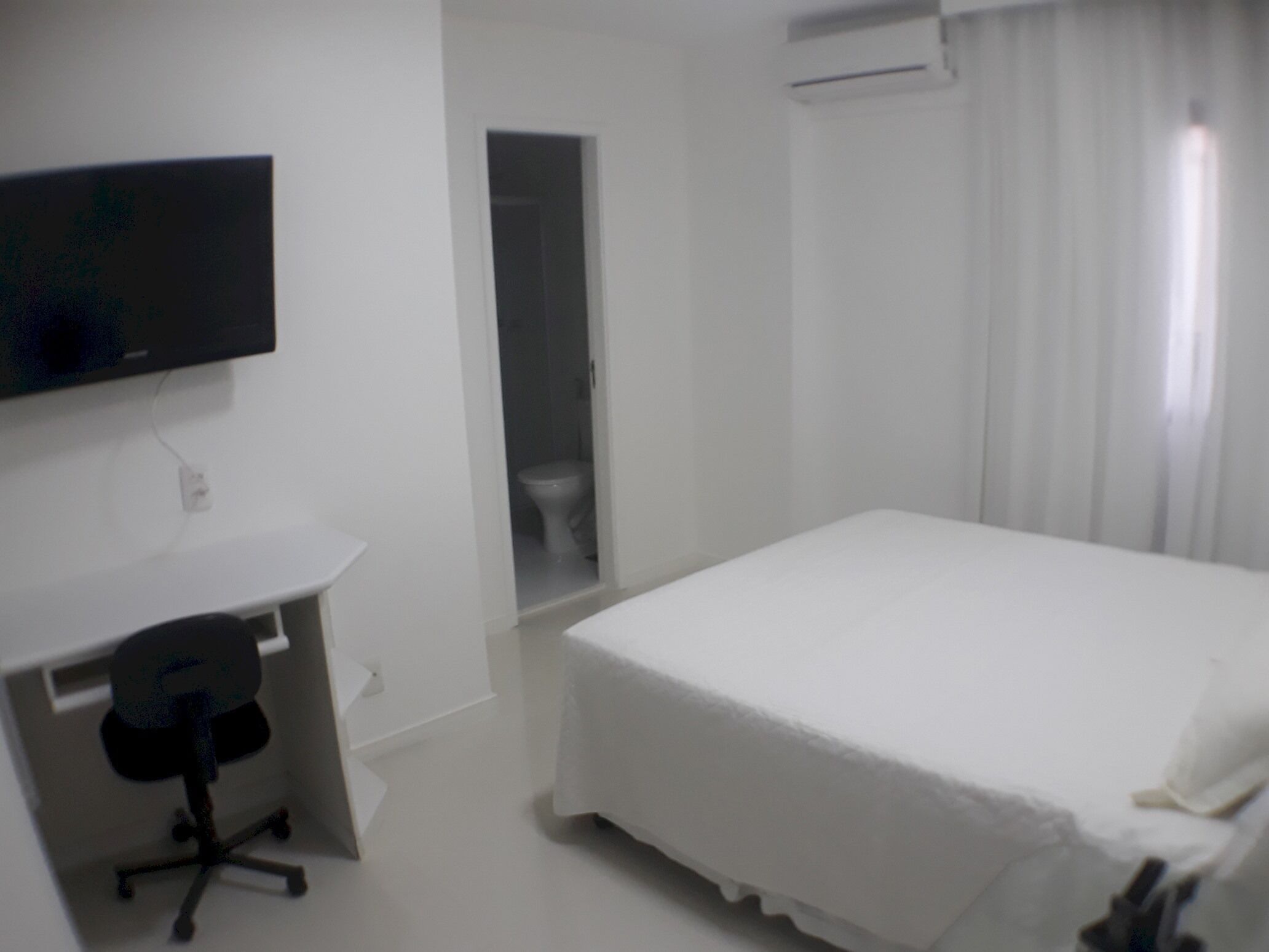Ein Hotelzimmer mit Bett, Schreibtisch mit Stuhl, Fernseher und einem durchgegangenen Tür erkennbaren Badezimmer.