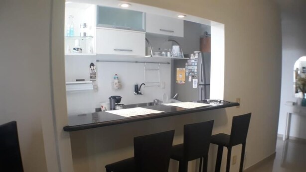 Cuina moderna amb taulell negre, tres tamborets i un frigorífic.