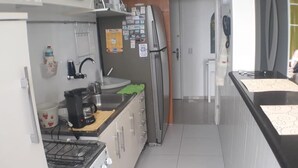 Una cuina compacta amb fogó de gas, cafetera, nevera i microones.