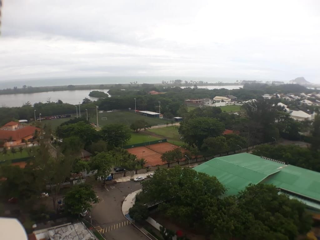 An aerial view of a residential area with a large green sports field, a tennis court, and a body of water in the background.