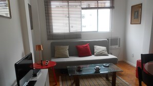 A living room with a sofa, a glass coffee table, a TV, and a red side table. - Gohouse - Torre 302 C (Rio de Janeiro)