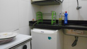 Una cocina compacta con estufa blanca, un refrigerador pequeño, un microondas y un lavamanos con grifo.