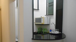 Un baño con un lavabo negro, un espejo, un microondas y una silla verde.