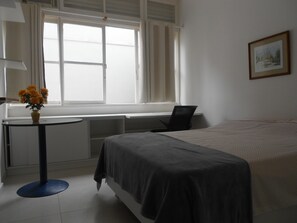 A hotel room with a bed, a desk, and a window.