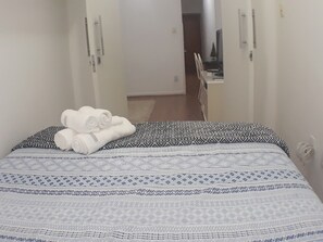 Una cama bien tendida con ropa de cama estampada, una toalla blanca enrollada y una mesita de noche con una lámpara.