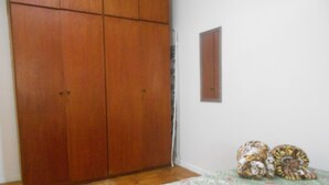 A bedroom with a wooden wardrobe, a bed with a floral bedspread, and a small wooden cabinet on the wall.