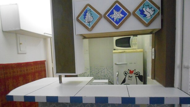 A bathroom with a white sink, a mirror, and a microwave above it. There are decorative tiles on the wall and a red patterned curtain.
